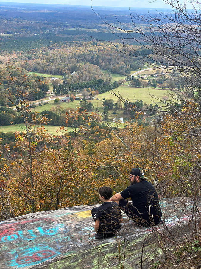 two people sitting on a cliff overlooking a landscape