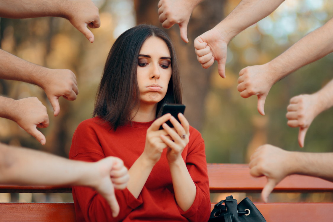 Woman pouting looking at her phone with several thumbs down around her.