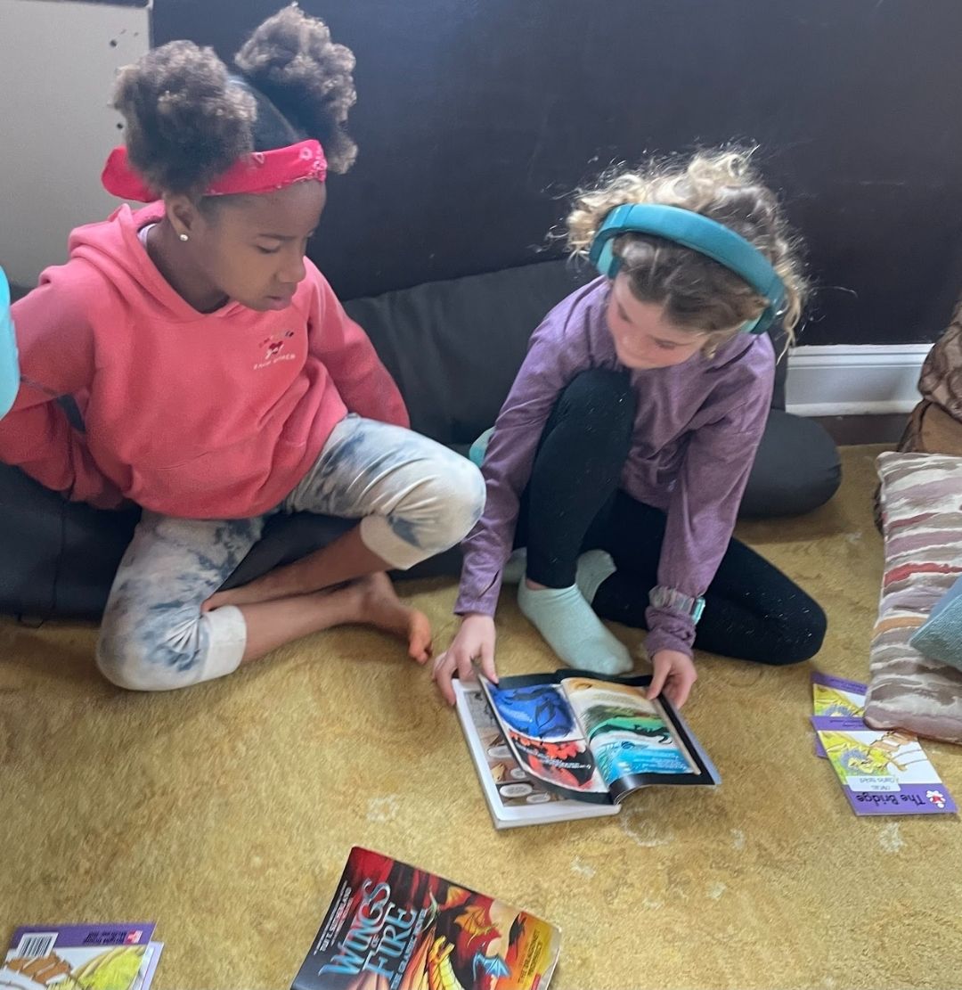 Roxy and her friend, Ava, reading <i>Wings of Fire</i> together with audio and graphic novel versions.