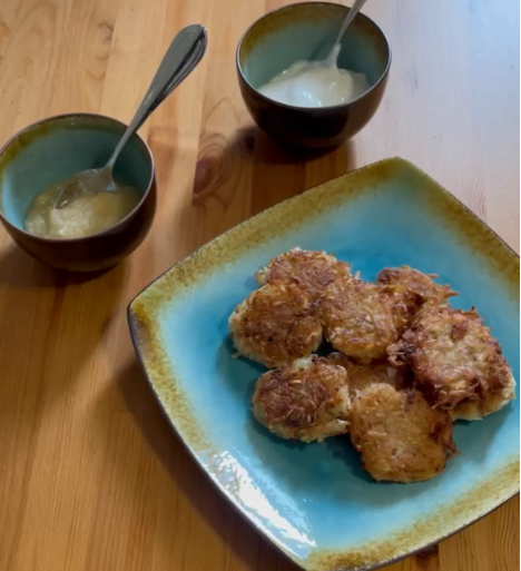 Potato latkes on a blue plate next to a small bowl of applesauce and sour cream